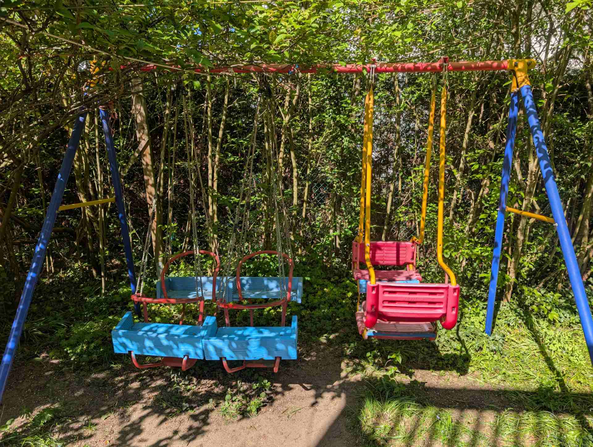 Bunte Kinderschaukel mit mehreren sicheren Sitzplätzen, idyllisch gelegen im Schatten unserer großen Bäume im Garten.
