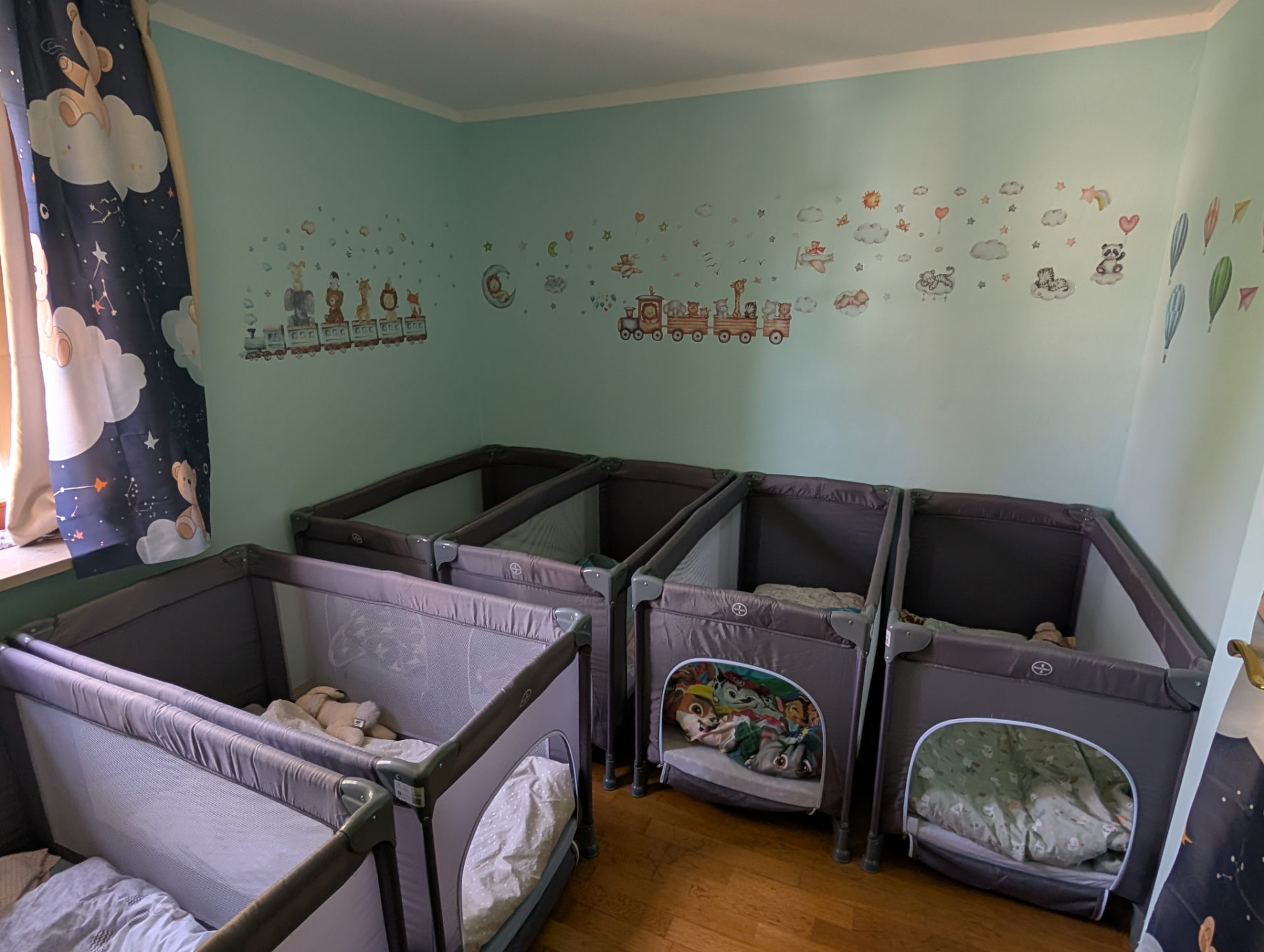 Ruhiger Schlafraum unserer Kindertagespflege mit gemütlichen Reisebettchen und niedlichen Tier-Wandtattoos für den entspannten Mittagsschlaf.